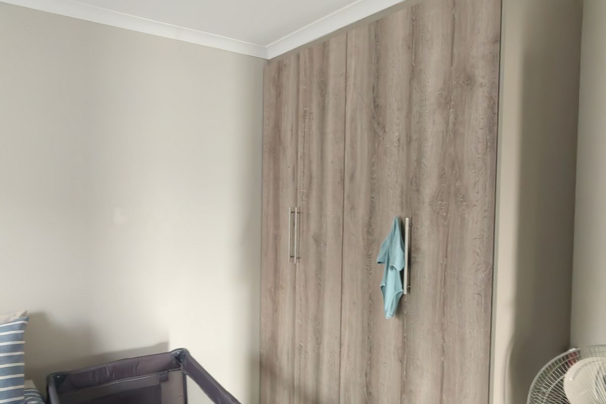 A bedroom featuring a modern wood-grain built-in wardrobe with sleek handles and recessed ceiling lighting.