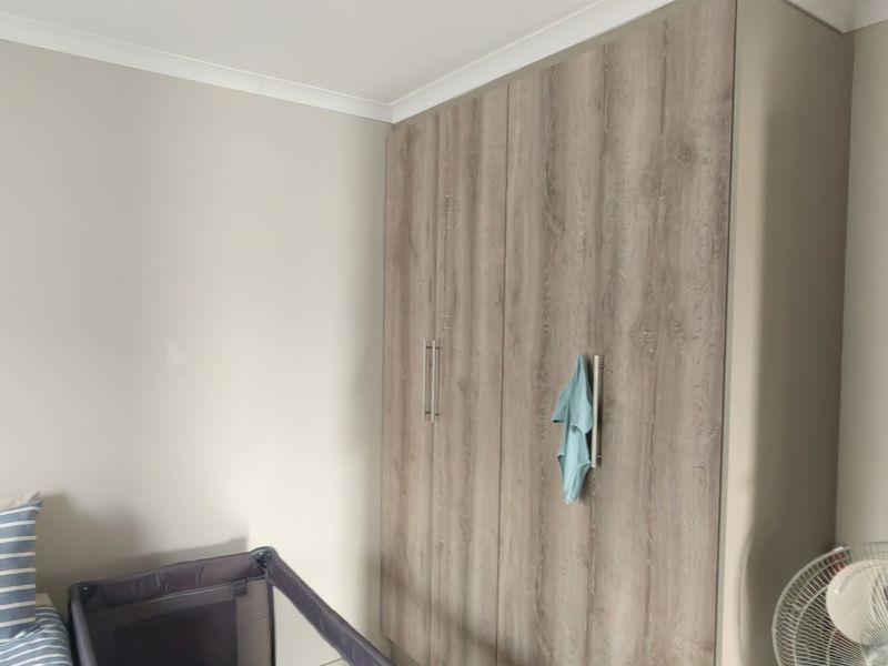 A bedroom featuring a modern wood-grain built-in wardrobe with sleek handles and recessed ceiling lighting.