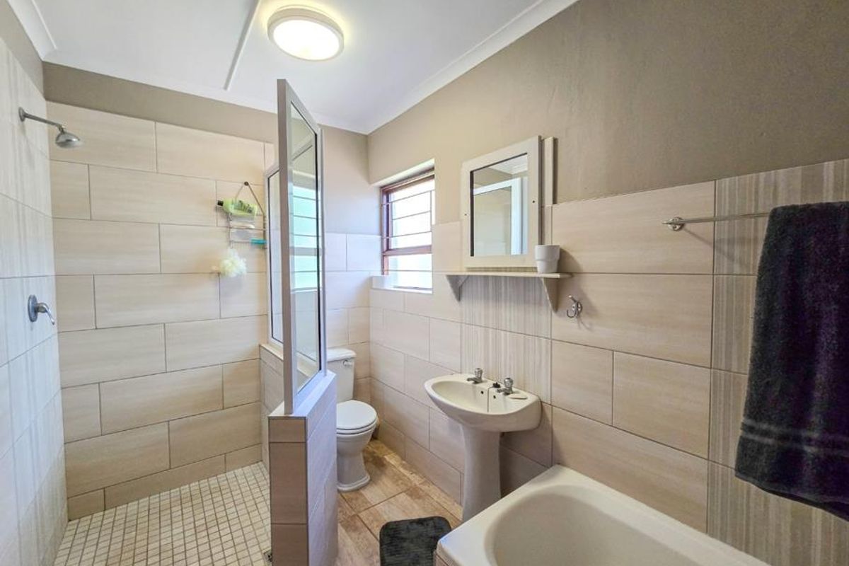 A well-maintained bathroom featuring a walk-in shower with glass partition, pedestal basin, toilet, and a bathtub with neutral wall tiling.