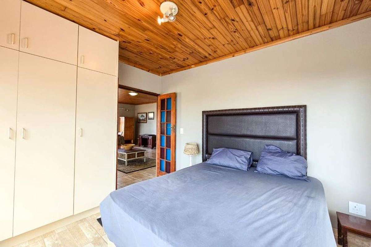 Bedroom featuring built-in cupboards, timber-clad ceiling, and tiled flooring, with an adjoining room visible through a decorative glass-panelled door.