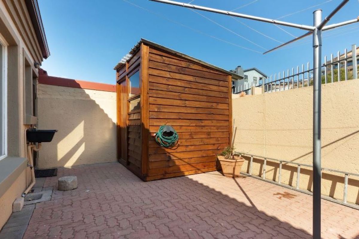 A paved rear courtyard featuring a wooden storage shed, an external wash basin, and a rotary clothesline, enclosed by a boundary wall.