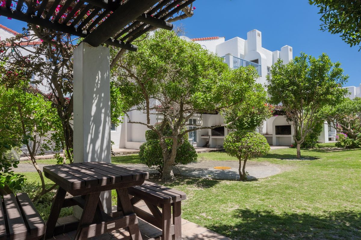 A well-maintained communal garden area featuring a paved patio, built-in braai facilities, and a shaded pergola, perfect for outdoor relaxation.