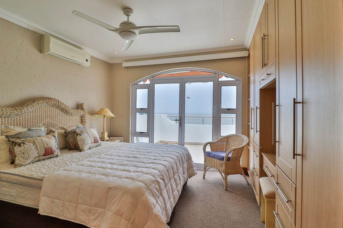 A well-maintained bedroom featuring built-in wooden cupboards, a ceiling fan, air conditioning, and direct access to a private balcony with ocean views.