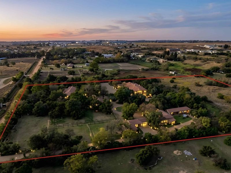 An expansive aerial view of a large residential estate featuring multiple buildings, mature trees, and a paved driveway within a clearly defined property boundary.