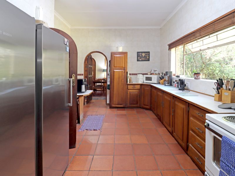 A functional kitchen featuring traditional wooden cabinetry, terracotta floor tiles, and a tiled splashback, offering a classic layout with ample storage space.