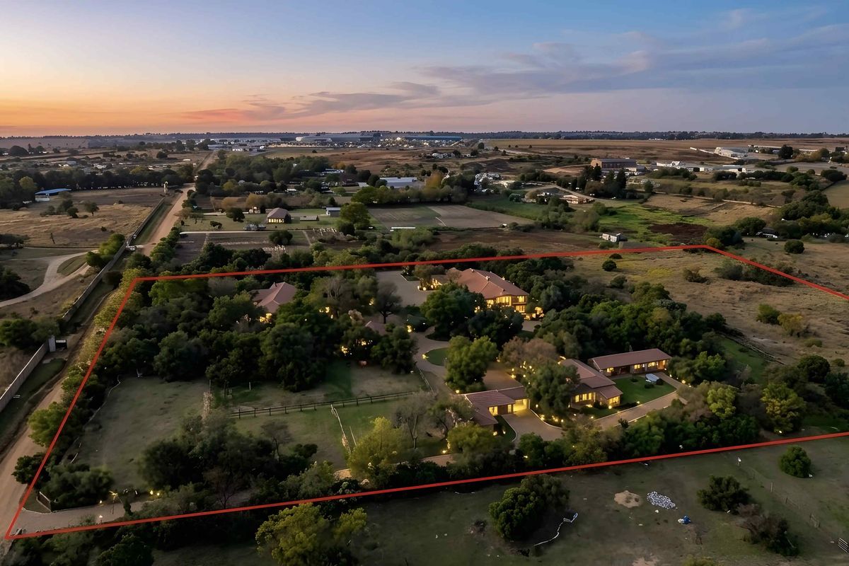 An expansive aerial view of a large residential estate featuring multiple buildings, mature trees, and a paved driveway within a clearly defined property boundary.