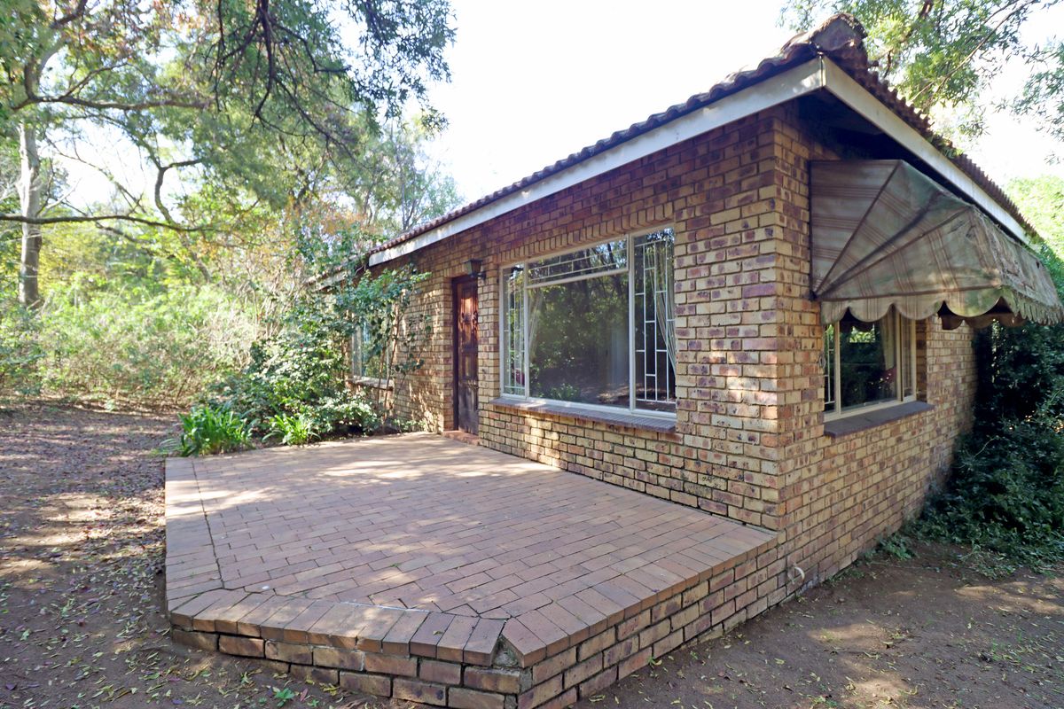 A rear view of a face brick house featuring a paved patio area, metal window frames, and a traditional tiled roof.