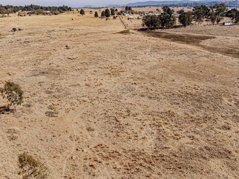 An aerial view of a large, open, dry residential vacant land plot with sparse vegetation and distant rural surroundings.