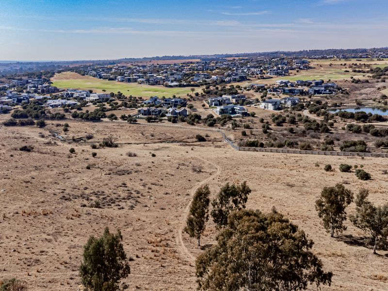 An aerial view of a large, undeveloped residential plot situated adjacent to an established estate with golf course and residential housing.