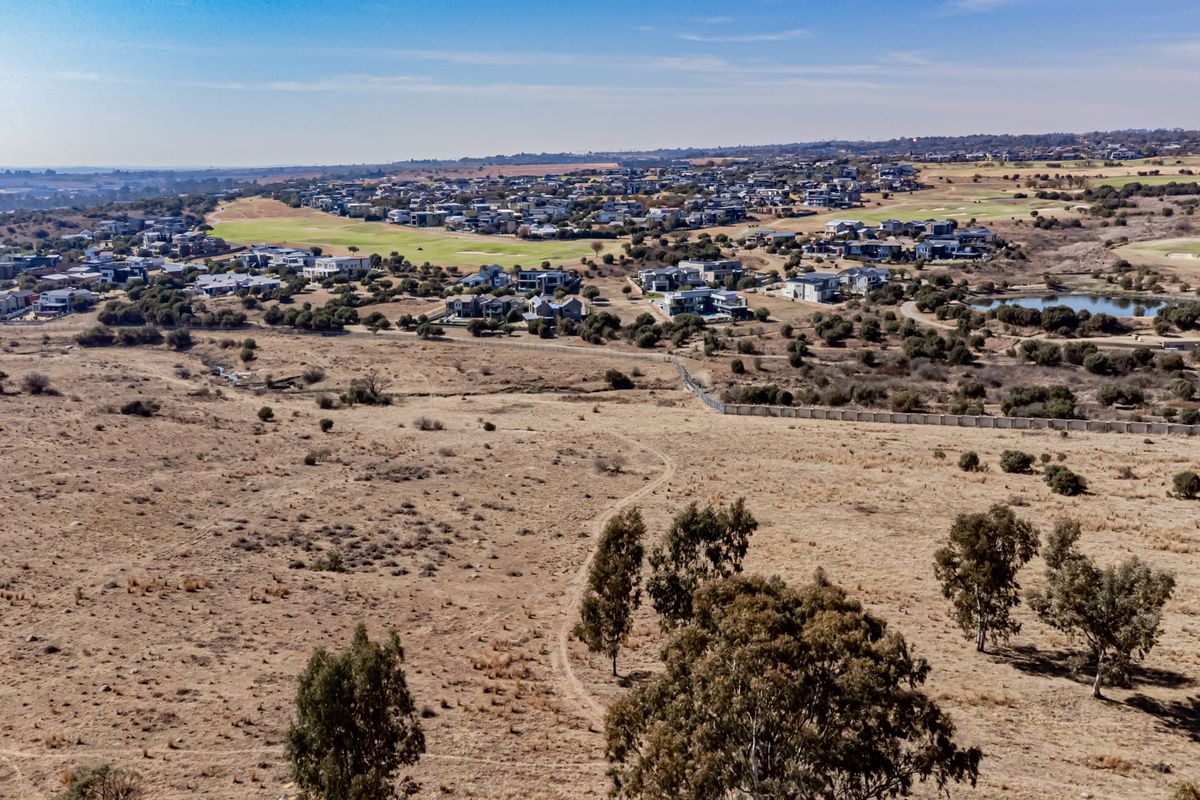 An aerial view of a large, undeveloped residential plot situated adjacent to an established estate with golf course and residential housing.