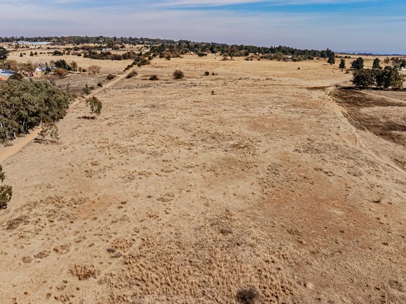 An aerial view of a large, expansive plot of vacant residential land featuring natural grass cover and scattered mature trees.