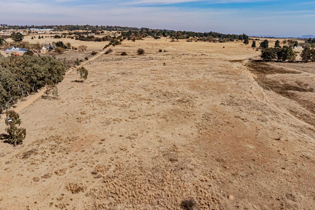 An aerial view of a large, expansive plot of vacant residential land featuring natural grass cover and scattered mature trees.