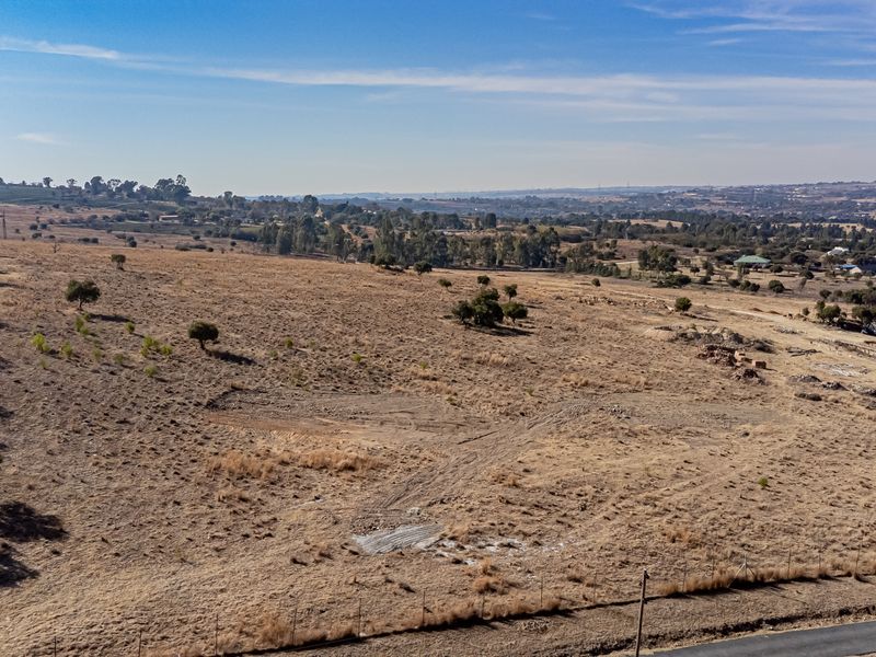 An aerial view of a large, vacant residential plot featuring dry grassland, perimeter wire fencing, and distant landscape views.