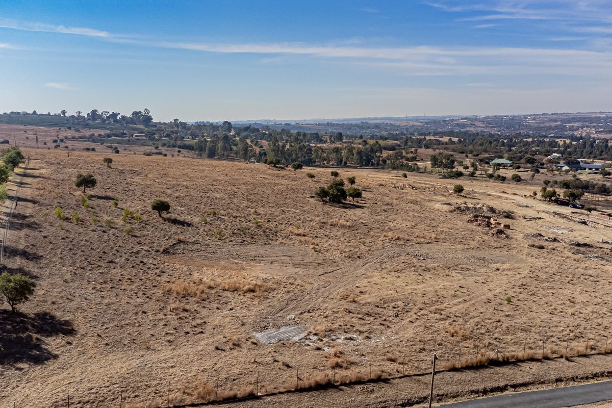 An aerial view of a large, vacant residential plot featuring dry grassland, perimeter wire fencing, and distant landscape views.