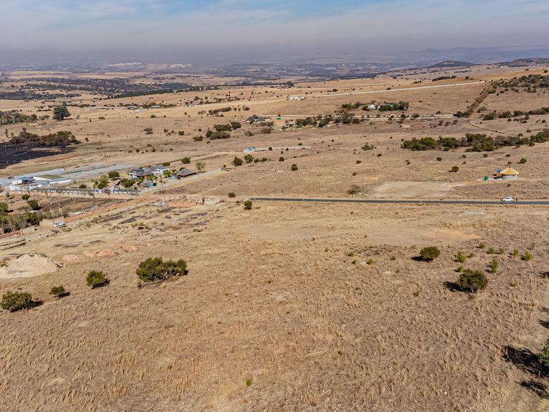 An aerial view of a large, vacant residential plot featuring natural landscape and surrounding rural terrain.