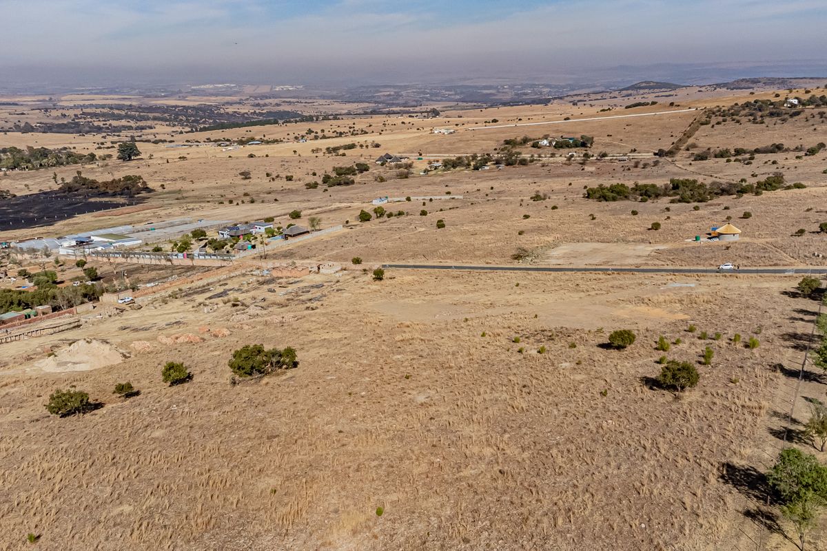 An aerial view of a large, vacant residential plot featuring natural landscape and surrounding rural terrain.