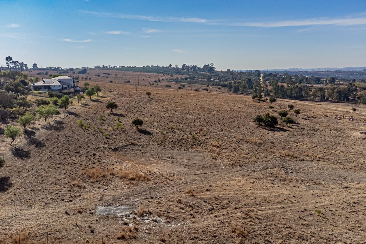 An aerial view of a large, open residential vacant land plot featuring natural vegetation and perimeter fencing.