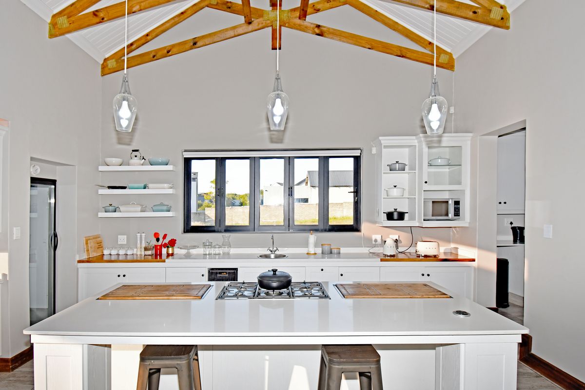 Modern kitchen featuring a central island with a built-in gas hob, white cabinetry, timber countertops, and exposed timber roof trusses.