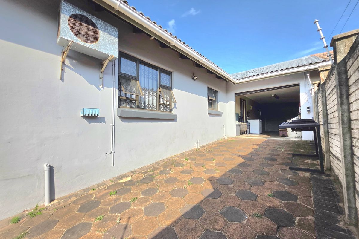 Rear exterior view of the property featuring a paved patio area, security-fitted windows, and an external air conditioning unit.