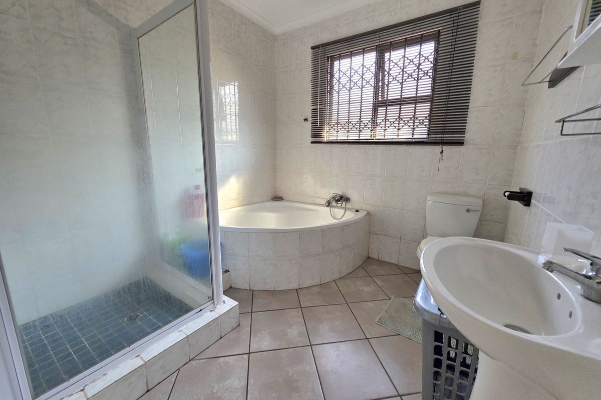 A functional bathroom featuring a corner bathtub, separate shower enclosure, pedestal basin, and toilet, finished with neutral wall and floor tiles.