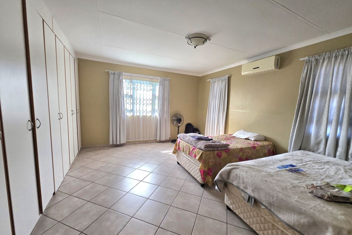 Spacious bedroom featuring tiled flooring, extensive built-in cupboards, and a wall-mounted air conditioning unit.
