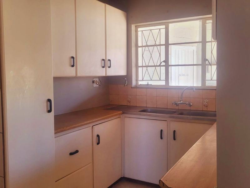 A functional kitchen featuring laminate countertops, a double basin sink, and ample built-in cabinetry with a tiled splashback and security-barred window.