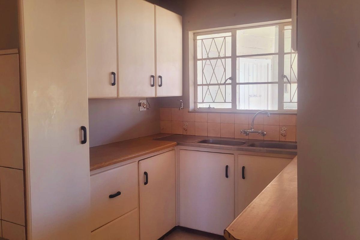 A functional kitchen featuring laminate countertops, a double basin sink, and ample built-in cabinetry with a tiled splashback and security-barred window.
