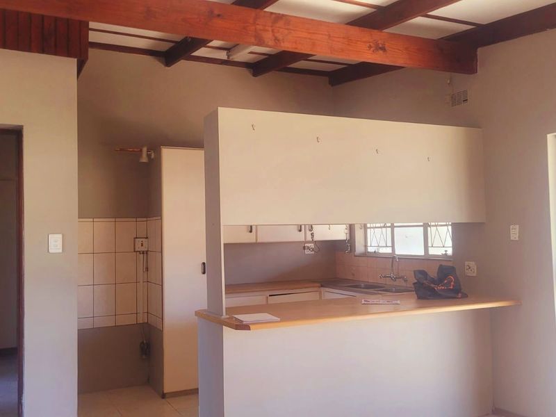 Open plan kitchen area featuring exposed timber ceiling beams, a breakfast bar, and built-in cabinetry with a tiled splashback.