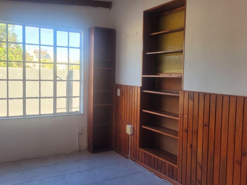 A bedroom featuring built-in wooden shelving, decorative timber wall paneling, tiled floors, and a large grid-style window providing natural light.