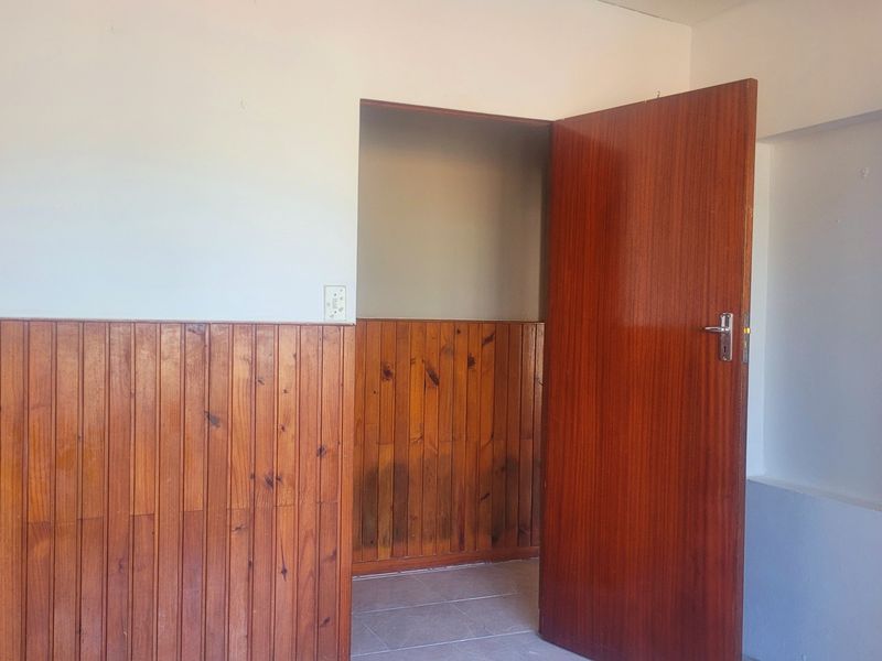 An empty bedroom featuring dated timber wall paneling, a solid wood door, and tiled flooring, offering a blank canvas for renovation.