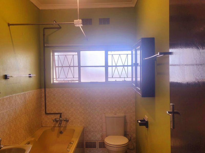 A dated bathroom featuring a bathtub, toilet, and washbasin with tiled splashbacks and window security bars, offering potential for modernization.