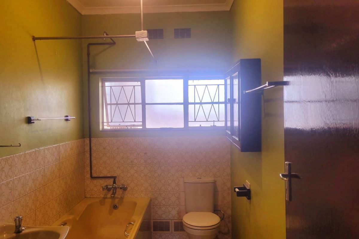 A dated bathroom featuring a bathtub, toilet, and washbasin with tiled splashbacks and window security bars, offering potential for modernization.