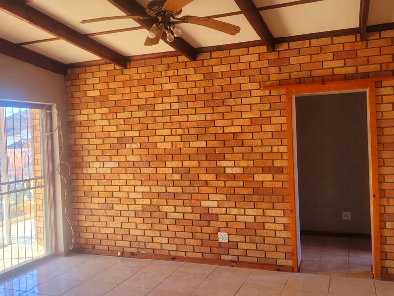 Spacious living area featuring an exposed brick feature wall, timber ceiling beams, ceiling fan, and large sliding glass doors leading to the exterior.