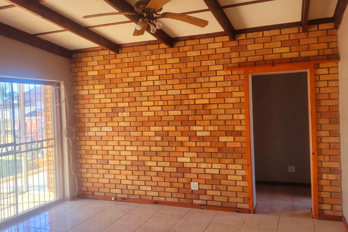 Spacious living area featuring an exposed brick feature wall, timber ceiling beams, ceiling fan, and large sliding glass doors leading to the exterior.