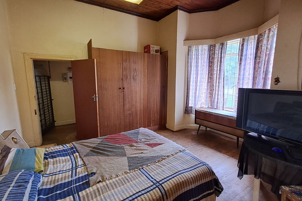 A bedroom featuring a bay window, built-in wooden wardrobe, and timber ceiling, offering a dated interior ready for modernization.