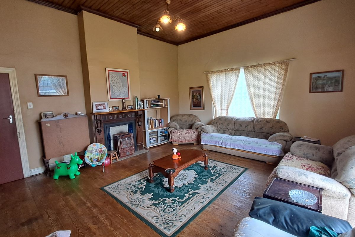 A spacious living room featuring a traditional fireplace with a mantelpiece, timber ceiling, and original timber flooring, offering a classic, dated aesthetic.