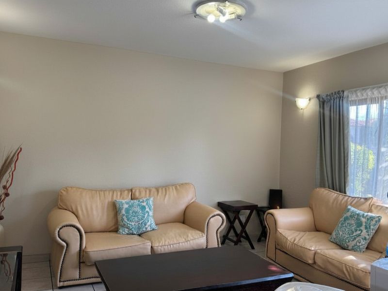 A neutrally painted living room featuring tiled flooring, a central ceiling light, and a wall-mounted sconce near the window.