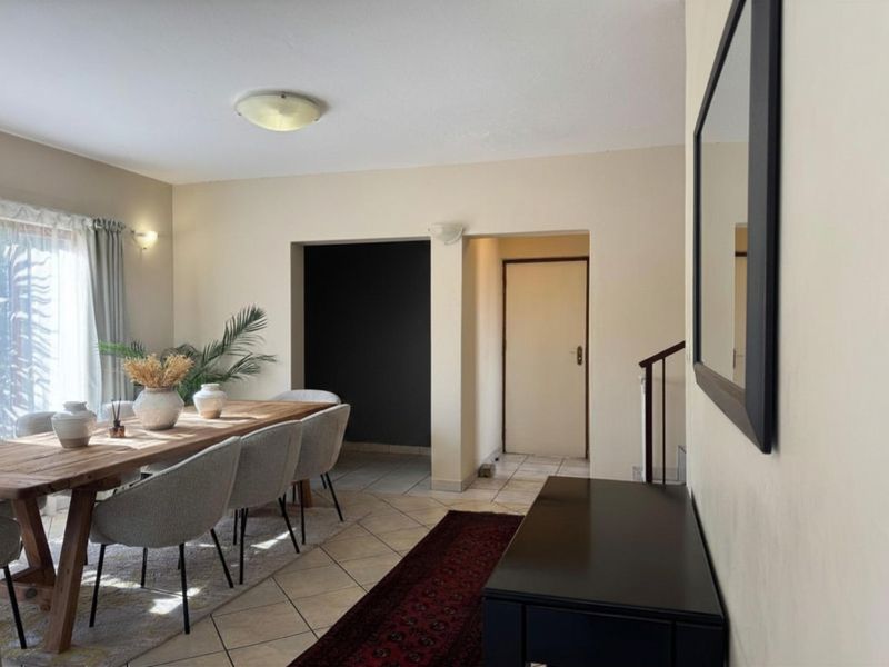 A dining area featuring tiled flooring and a neutral color palette, with an open transition to a hallway and staircase.