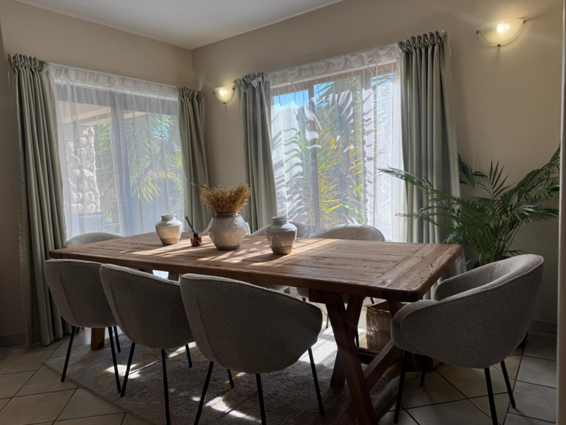 A bright dining room featuring tiled flooring, wall-mounted lighting, and large sliding glass doors that provide ample natural light.