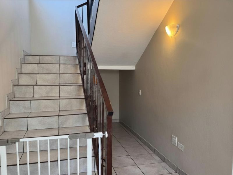 A bright, tiled hallway featuring a staircase with a decorative wrought iron balustrade and wall-mounted lighting.