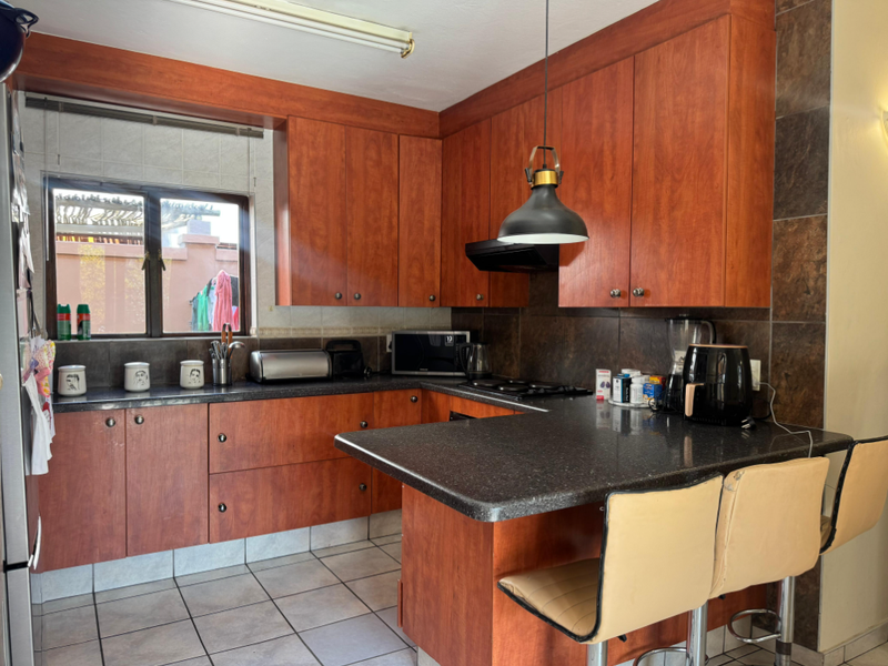 A functional kitchen featuring warm-toned wooden cabinetry, dark granite countertops, a built-in hob with extractor, and tiled flooring throughout.