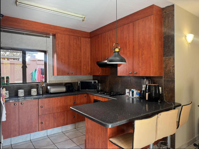 A functional kitchen featuring wood-finish cabinetry, dark countertops, a breakfast bar, and tiled flooring, offering a practical layout for daily use.