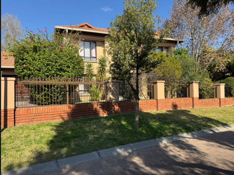 Front view of a two-story residential house featuring a brick and wrought iron boundary wall, tiled roof, and established garden.