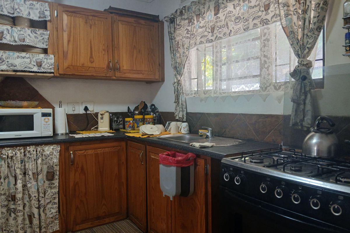 A functional kitchen featuring traditional wooden cabinetry, laminate countertops, a stainless steel sink, and a gas stove with a tiled backsplash.