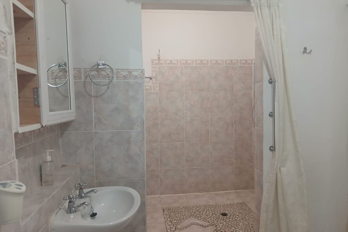 A functional bathroom featuring a pedestal washbasin, medicine cabinet, and a tiled shower enclosure with a curtain rail.