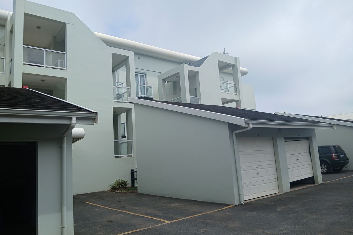 Exterior view of the apartment complex featuring multiple garages, paved driveway, and private balconies with glass balustrades.
