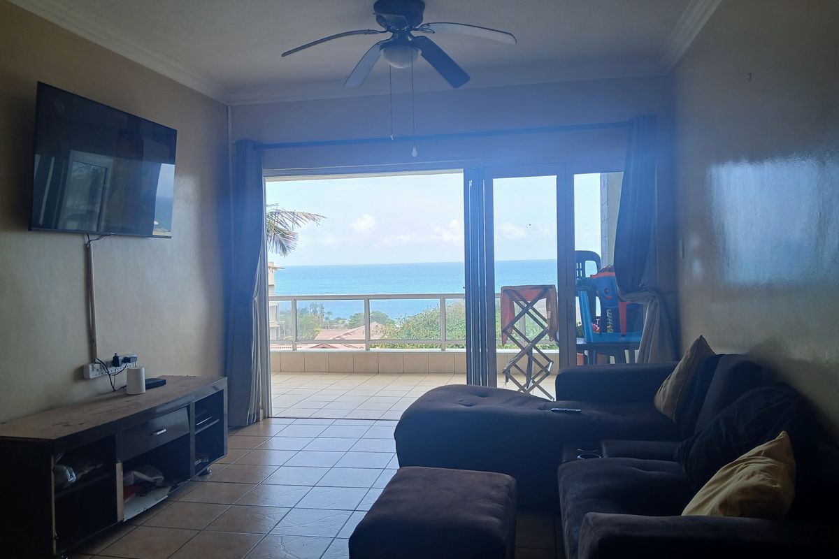 Living room featuring tiled floors, a ceiling fan, and large sliding glass doors opening onto a balcony with ocean views.