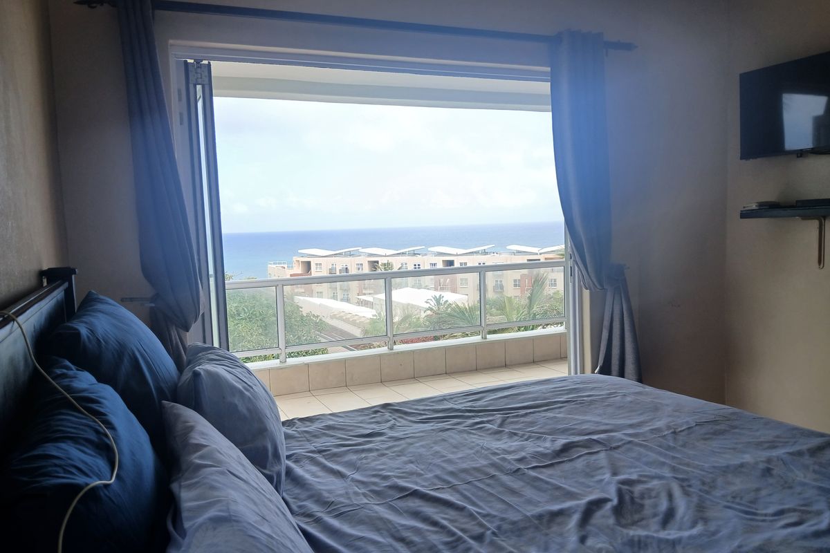 A bedroom featuring a balcony with a glass balustrade and ocean views, equipped with a ceiling fan.