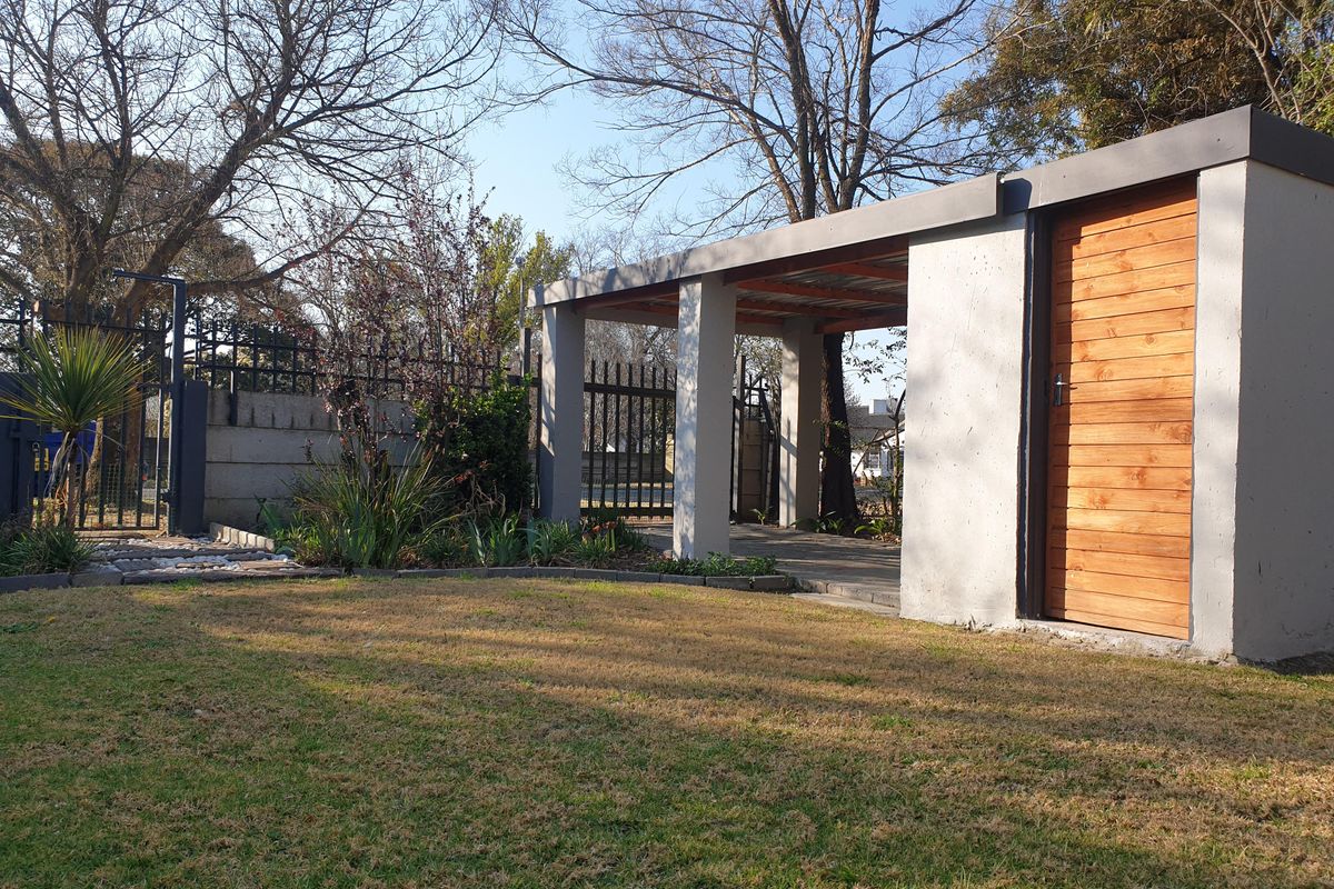 A well-maintained rear garden featuring a modern carport with concrete pillars and an integrated timber-clad storage unit, complemented by established landscaping and perimeter fencing.