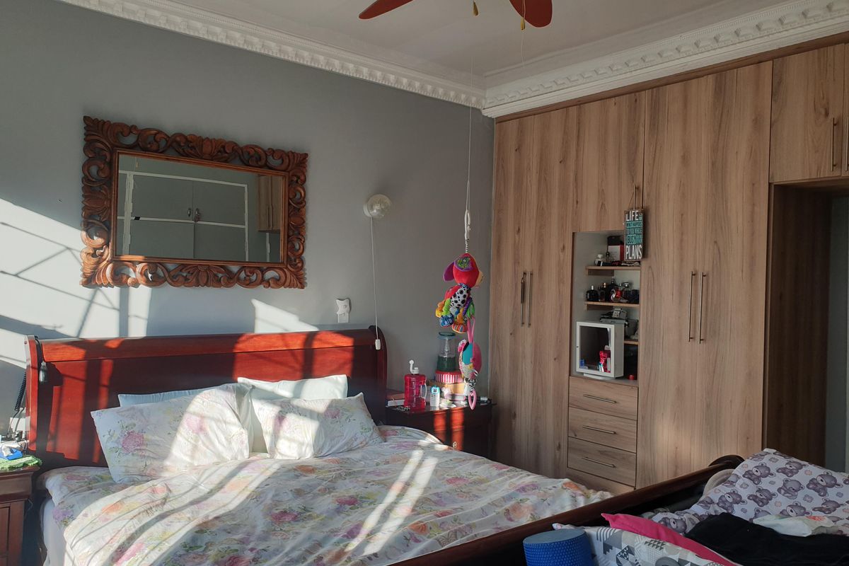 A well-lit bedroom featuring extensive built-in wooden cupboards, a ceiling fan, and decorative crown molding.